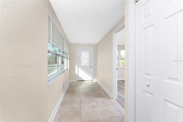 hall featuring light tile patterned floors, a textured ceiling, and a healthy amount of sunlight