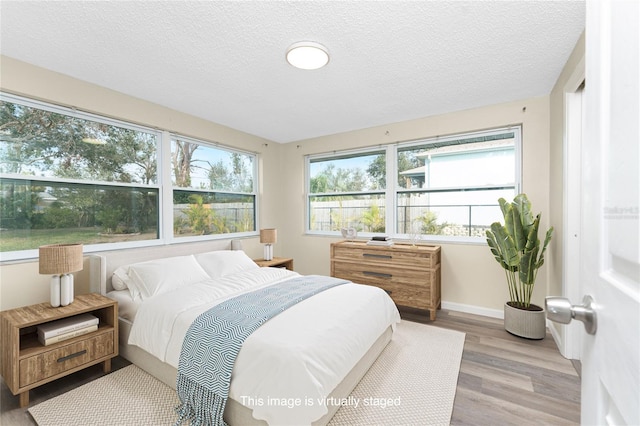 bedroom featuring baseboards, a textured ceiling, and light wood finished floors