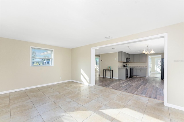 unfurnished living room featuring a notable chandelier, plenty of natural light, visible vents, and light tile patterned floors