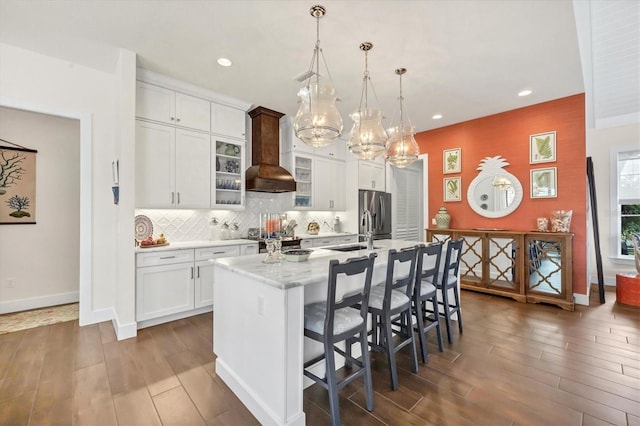 kitchen featuring stainless steel fridge, an island with sink, pendant lighting, a breakfast bar area, and custom range hood