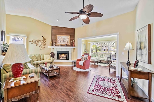 living room with hardwood / wood-style floors, ceiling fan, a tiled fireplace, and vaulted ceiling