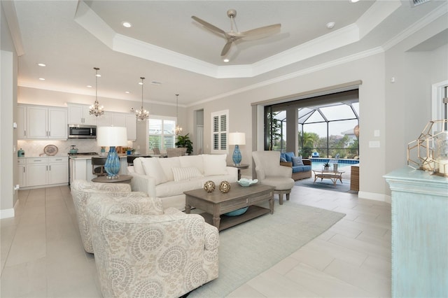 living room featuring ceiling fan with notable chandelier, light tile patterned flooring, ornamental molding, and a tray ceiling