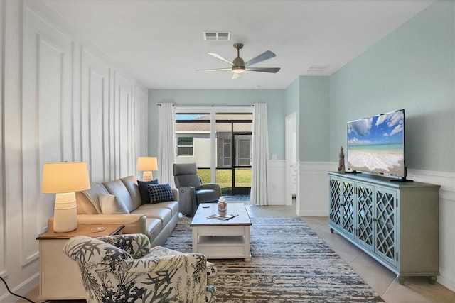 living room featuring light tile patterned floors, a wainscoted wall, visible vents, and a ceiling fan