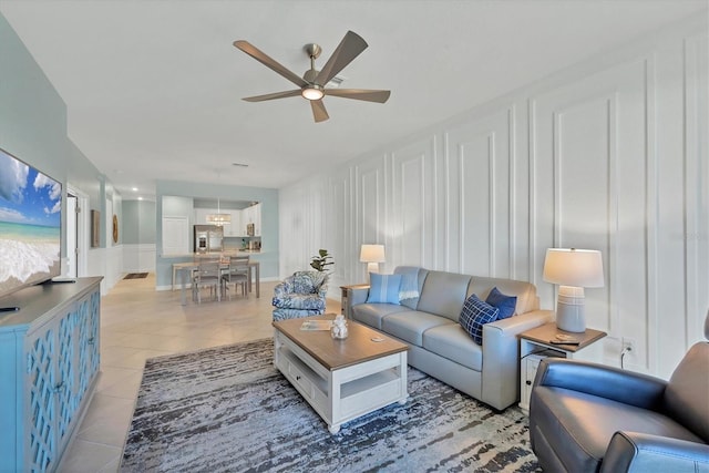 living area with a decorative wall, a ceiling fan, and light tile patterned flooring