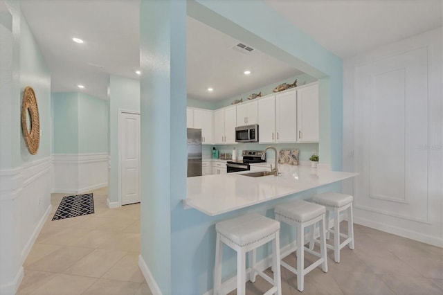 kitchen featuring stainless steel appliances, a peninsula, a kitchen breakfast bar, white cabinets, and light countertops