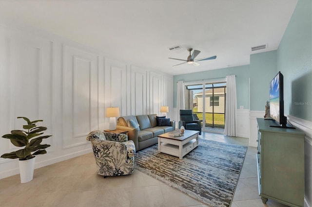 living area featuring light tile patterned floors, visible vents, a decorative wall, and a ceiling fan