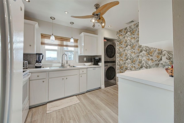 kitchen with backsplash, white appliances, sink, stacked washer / dryer, and white cabinets