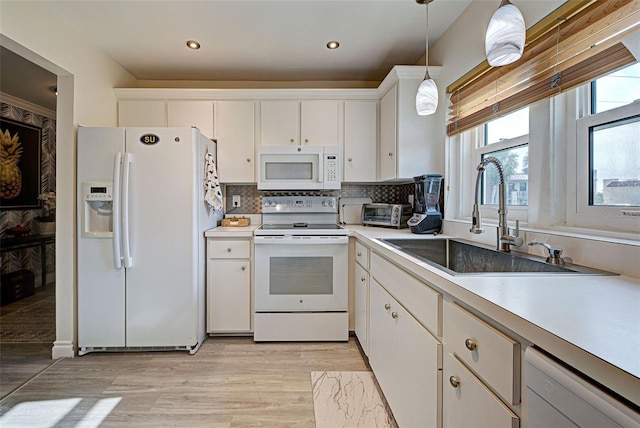 kitchen with white appliances, sink, light hardwood / wood-style floors, white cabinetry, and hanging light fixtures