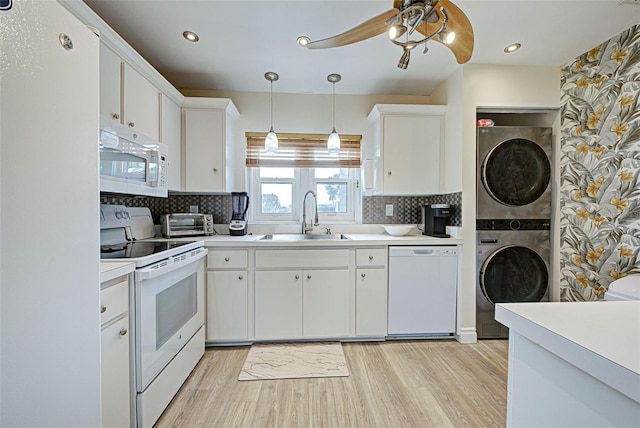 kitchen featuring sink, decorative light fixtures, white appliances, white cabinets, and stacked washer and clothes dryer