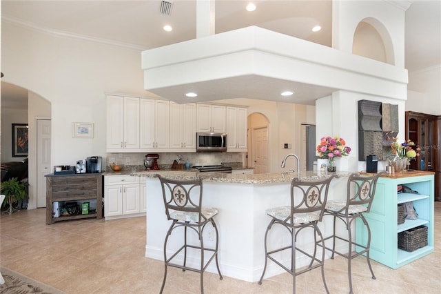 kitchen with white cabinetry, light stone counters, backsplash, stove, and a breakfast bar area