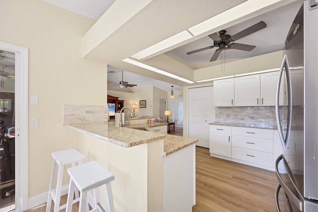 kitchen with kitchen peninsula, backsplash, stainless steel refrigerator, and light stone counters