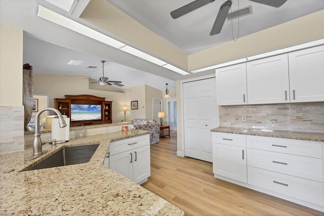 kitchen with decorative backsplash, light stone countertops, vaulted ceiling, sink, and white cabinets