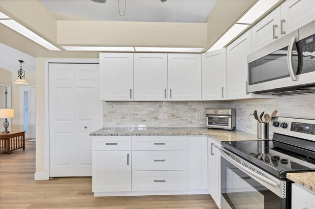 kitchen with appliances with stainless steel finishes, backsplash, light stone counters, pendant lighting, and white cabinets