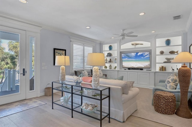 living room featuring built in shelves, light hardwood / wood-style floors, ceiling fan, and ornamental molding