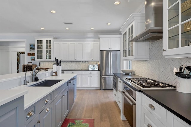 kitchen with appliances with stainless steel finishes, sink, white cabinetry, and wall chimney range hood