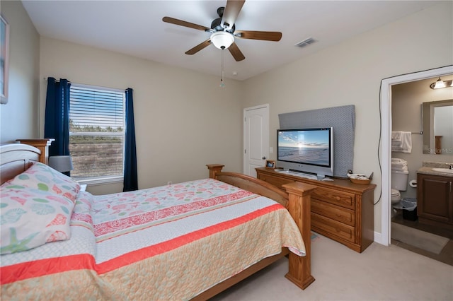 bedroom featuring ceiling fan, ensuite bathroom, and light colored carpet