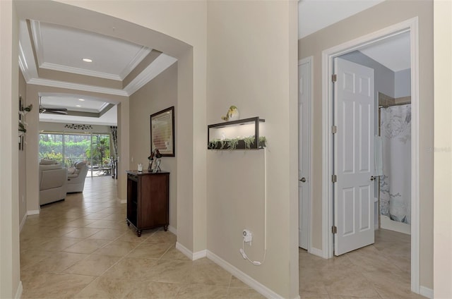 corridor featuring a tray ceiling, crown molding, and light tile patterned floors