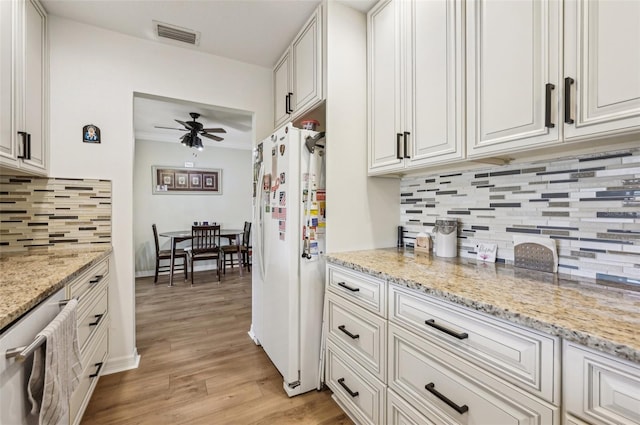 kitchen featuring light stone countertops, light wood-type flooring, ceiling fan, white refrigerator, and white cabinetry