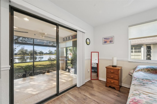 bedroom with multiple windows, a water view, and light wood-type flooring