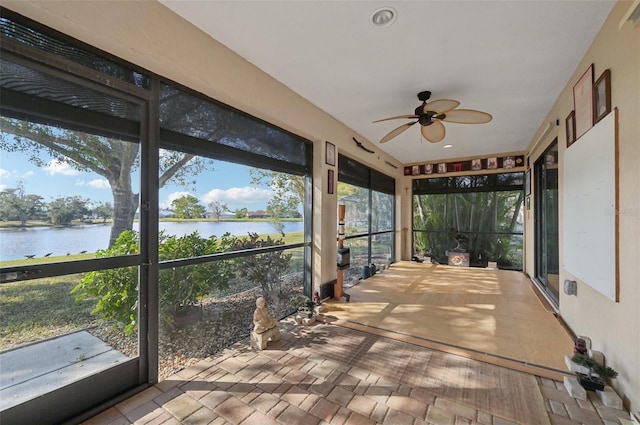 sunroom featuring ceiling fan and a water view