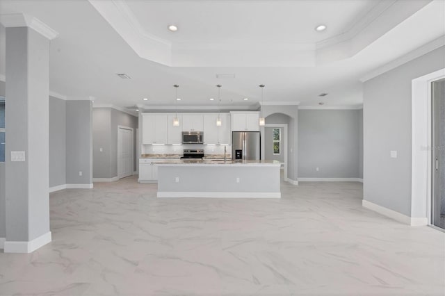 kitchen featuring white cabinets, an island with sink, appliances with stainless steel finishes, a tray ceiling, and decorative light fixtures