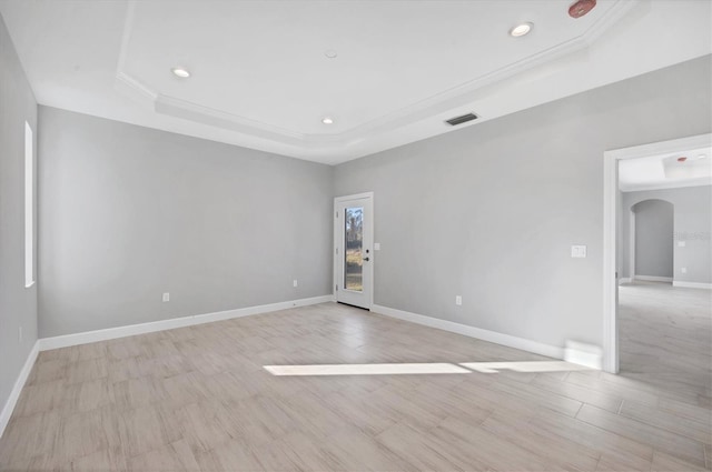 spare room featuring plenty of natural light, a raised ceiling, light wood-type flooring, and crown molding