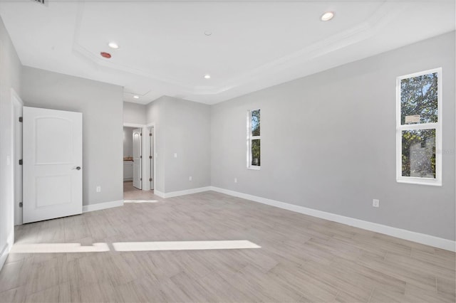 unfurnished bedroom with a tray ceiling, light hardwood / wood-style flooring, and multiple windows