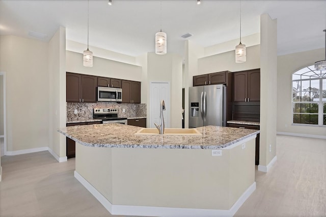 kitchen featuring a kitchen island with sink, hanging light fixtures, sink, appliances with stainless steel finishes, and dark brown cabinetry