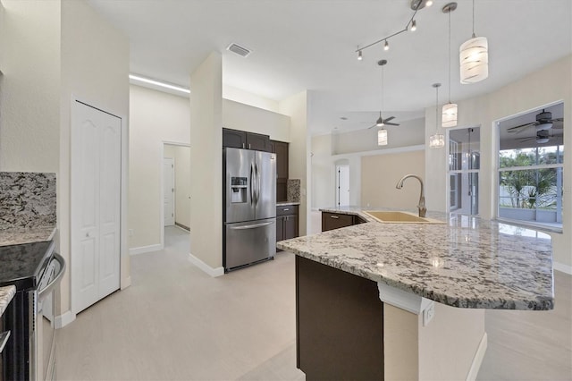 kitchen with sink, stainless steel appliances, light stone counters, pendant lighting, and a kitchen island with sink