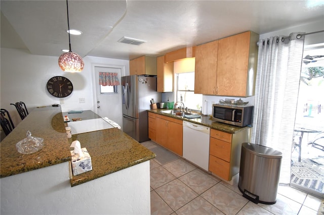 kitchen featuring dark stone counters, hanging light fixtures, sink, light tile patterned floors, and appliances with stainless steel finishes