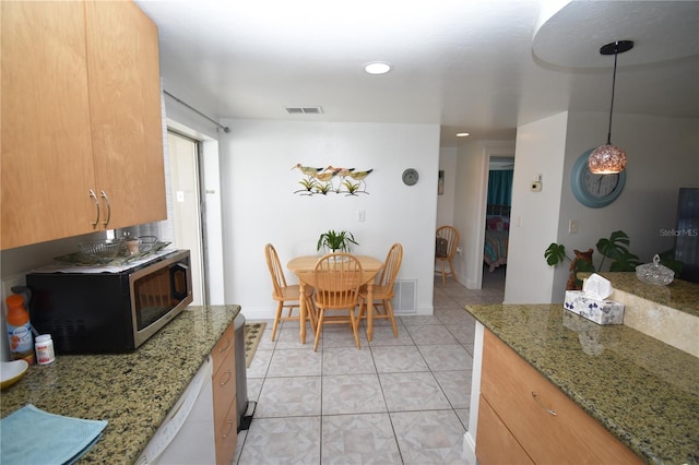 kitchen featuring white dishwasher, decorative light fixtures, light tile patterned floors, and stone counters