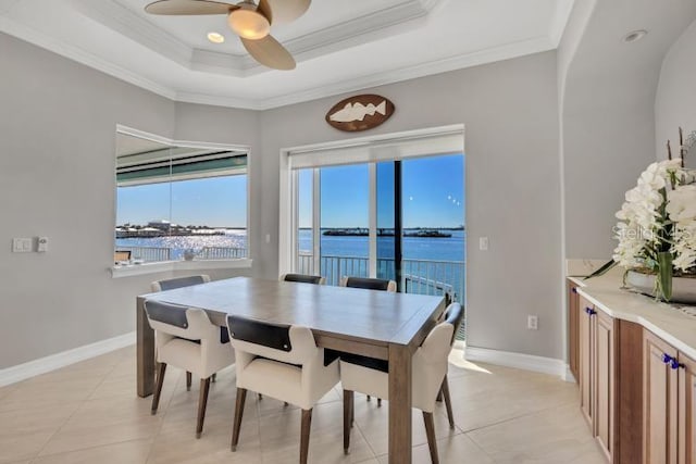 dining space featuring a raised ceiling, ceiling fan, crown molding, light tile patterned floors, and a water view