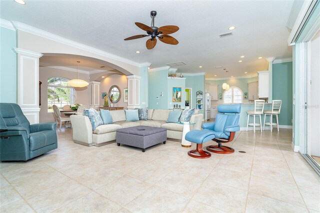 tiled living room featuring ornate columns, ceiling fan, and crown molding