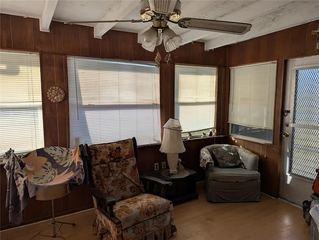 sitting room featuring beamed ceiling, light hardwood / wood-style floors, ceiling fan, and wood walls