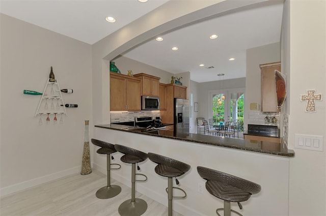 kitchen with dark stone countertops, kitchen peninsula, decorative backsplash, hanging light fixtures, and appliances with stainless steel finishes