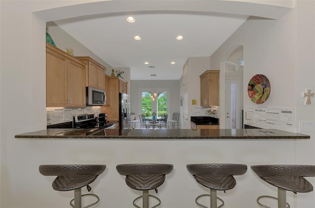 kitchen with appliances with stainless steel finishes, hanging light fixtures, kitchen peninsula, dark stone counters, and backsplash