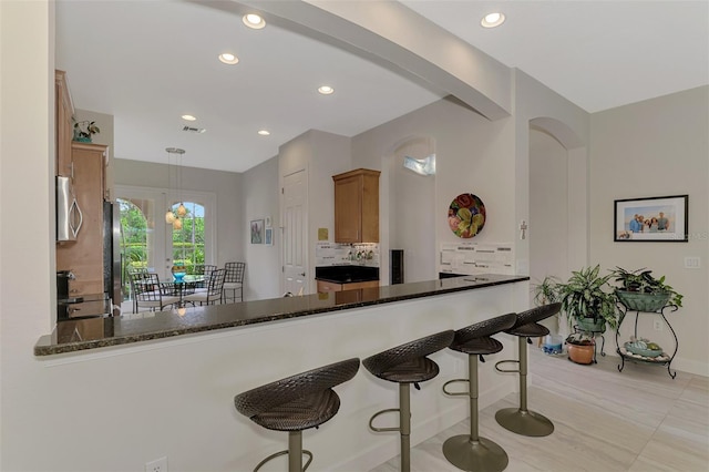 kitchen featuring kitchen peninsula, hanging light fixtures, tasteful backsplash, dark stone countertops, and stove