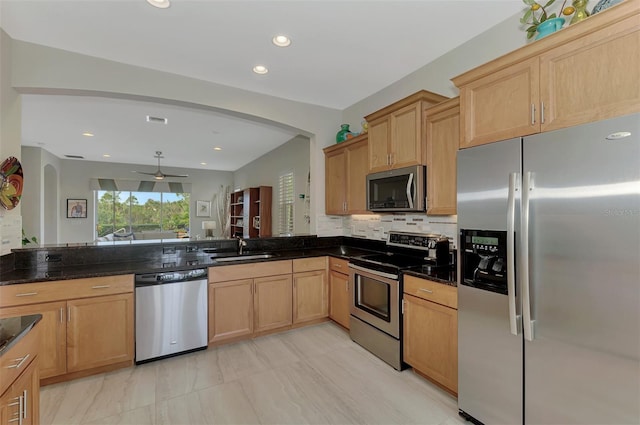 kitchen with sink, ceiling fan, backsplash, dark stone counters, and appliances with stainless steel finishes