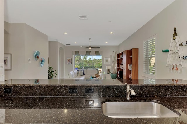 kitchen with ceiling fan, dark stone countertops, and sink