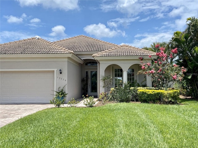 mediterranean / spanish home featuring a tile roof, a front lawn, a garage, stucco siding, and decorative driveway