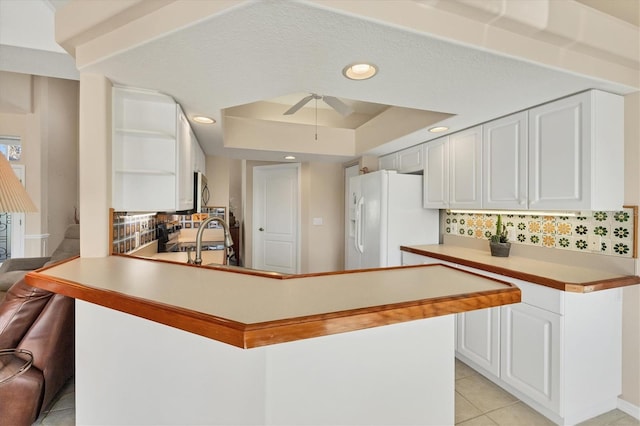 kitchen featuring white cabinetry, white fridge with ice dispenser, ceiling fan, kitchen peninsula, and decorative backsplash