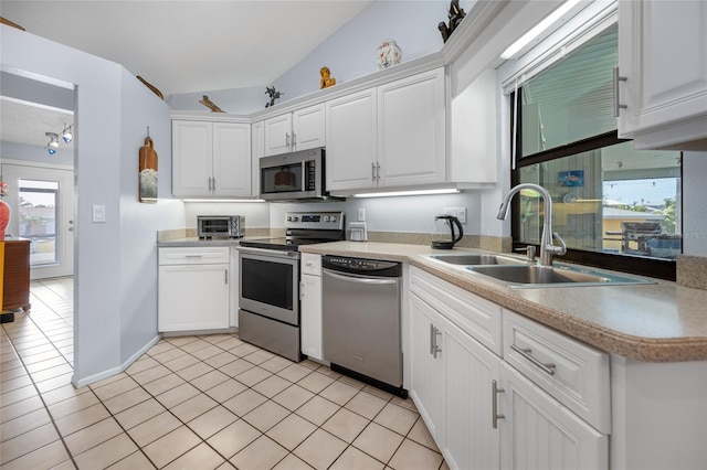 kitchen featuring sink, stainless steel appliances, light tile patterned floors, lofted ceiling, and white cabinets