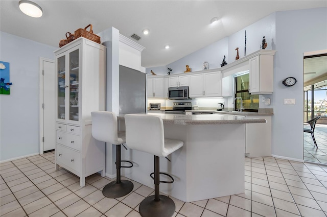 kitchen featuring sink, light tile patterned flooring, a kitchen bar, white cabinets, and appliances with stainless steel finishes