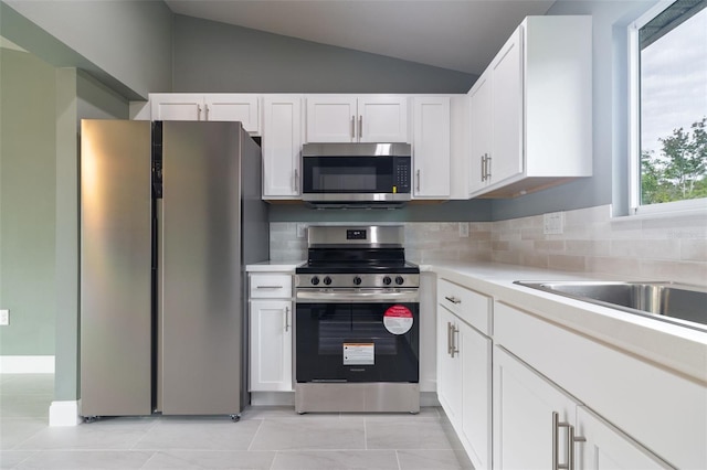 kitchen featuring stainless steel appliances, white cabinets, backsplash, lofted ceiling, and light tile patterned floors