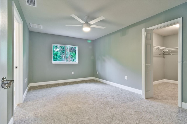 unfurnished bedroom featuring ceiling fan, light colored carpet, a walk in closet, and a closet