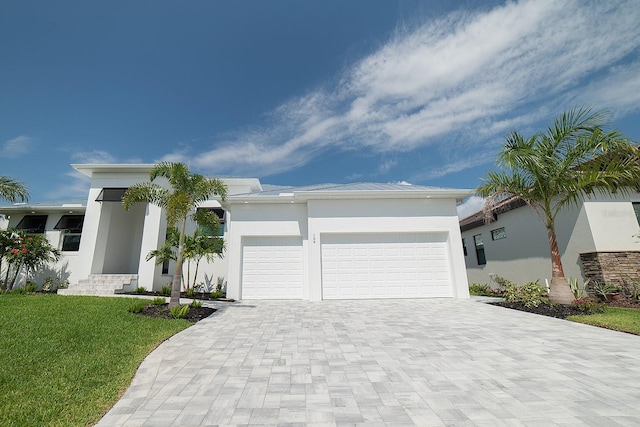 view of front of property featuring decorative driveway, a front lawn, an attached garage, and stucco siding