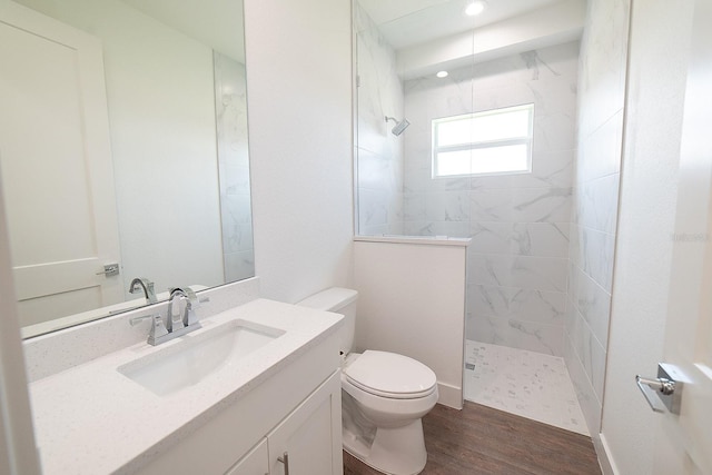 bathroom with hardwood / wood-style floors, vanity, toilet, and tiled shower