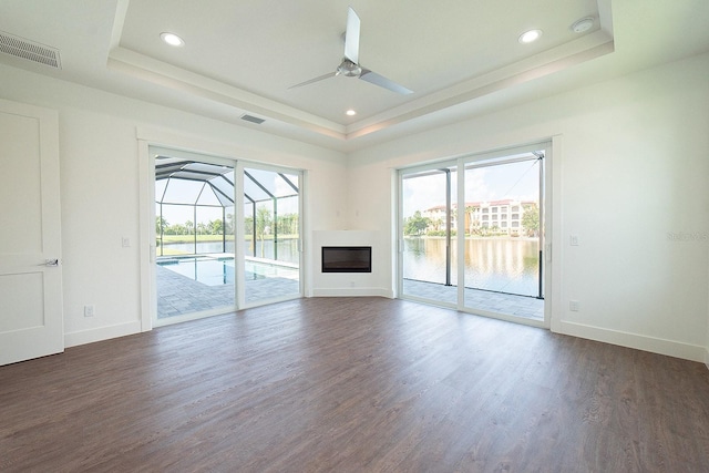 unfurnished living room featuring a raised ceiling, ceiling fan, a water view, and dark hardwood / wood-style floors