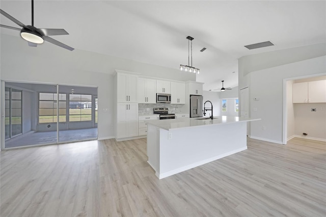 kitchen with a center island with sink, hanging light fixtures, light hardwood / wood-style floors, white cabinetry, and stainless steel appliances