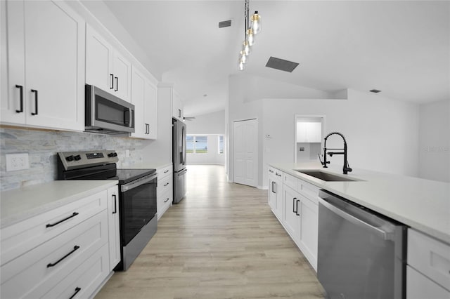 kitchen featuring sink, hanging light fixtures, stainless steel appliances, vaulted ceiling, and white cabinets